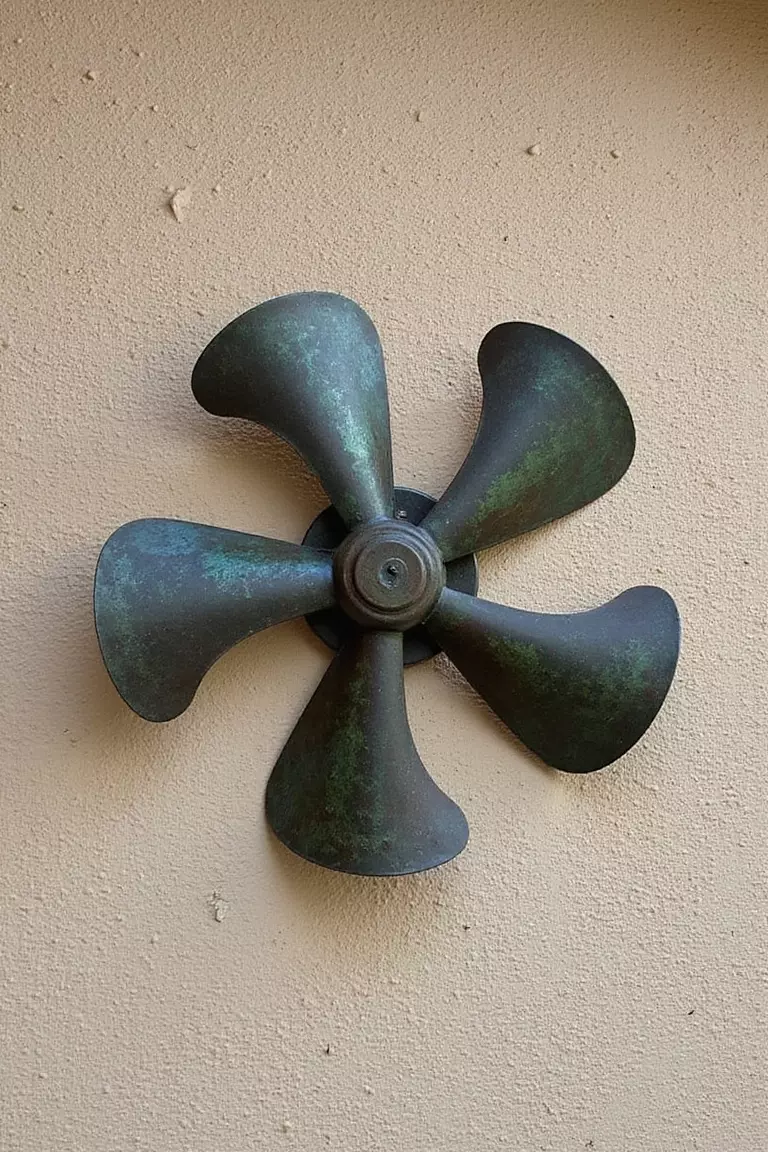 Decorative Outdoor Fan A close-up photo of a typical American home's garden wall with a large decorative metal fan with patina finish mounted as art piece against stucco background.