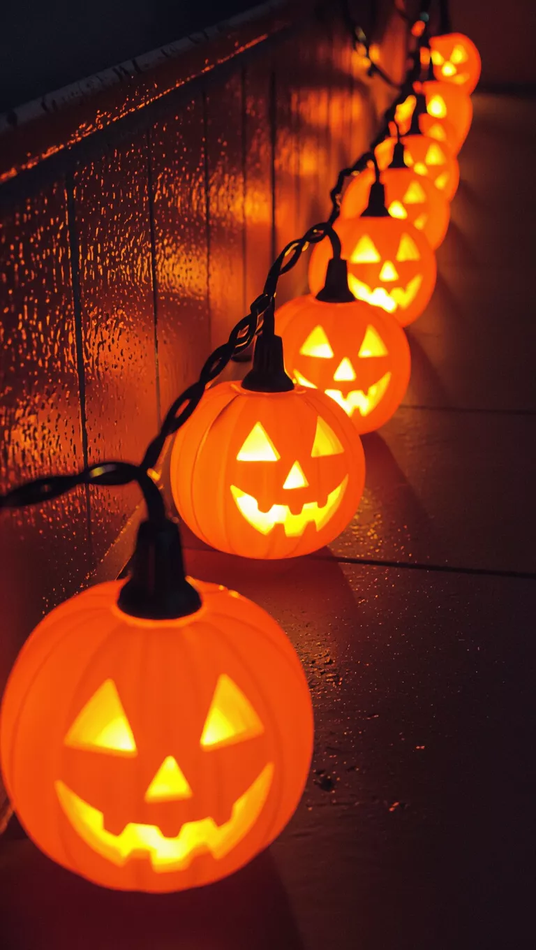 A photo of a string of glowing, orange jack-o'-lantern lights illuminates a dark space, creating a warm and festive Halloween atmosphere.